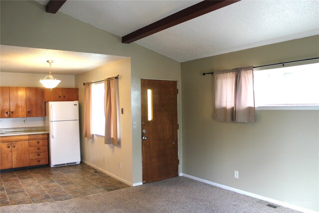 kitchen featuring plenty of natural light, lofted ceiling with beams, pendant lighting, white refrigerator, and dark tile floors