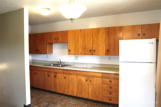 kitchen featuring white refrigerator, sink, dark tile floors, and a textured ceiling