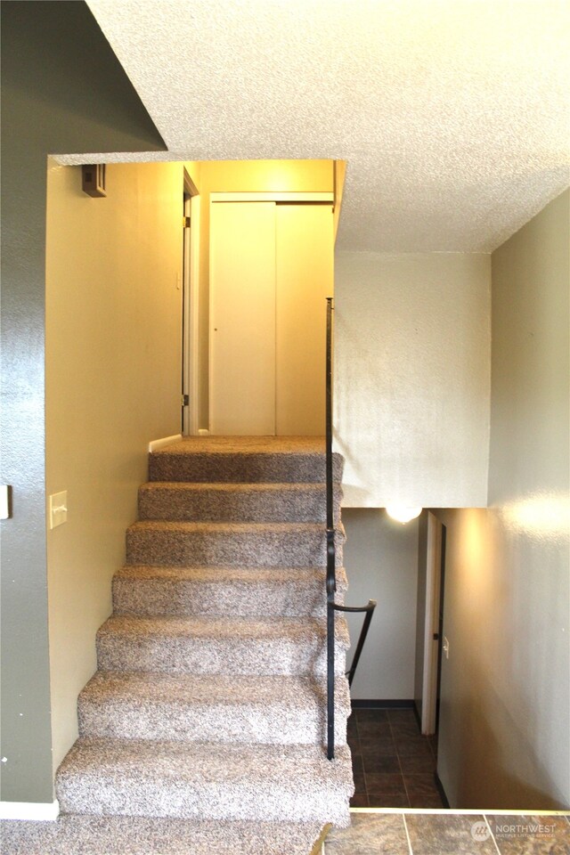 stairway featuring dark tile flooring and a textured ceiling