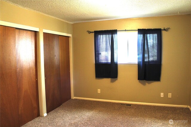 unfurnished bedroom featuring a textured ceiling, carpet floors, and two closets