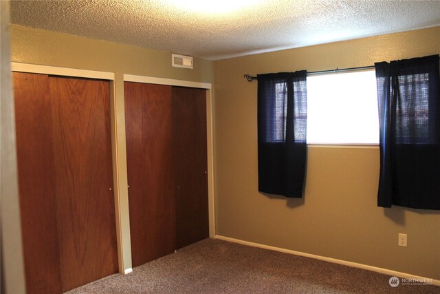 unfurnished bedroom with two closets, carpet floors, and a textured ceiling