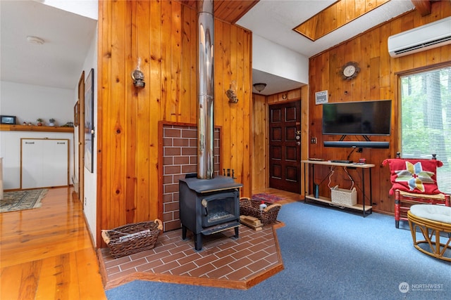 living room with a wall mounted AC, wooden walls, a wood stove, and hardwood / wood-style floors