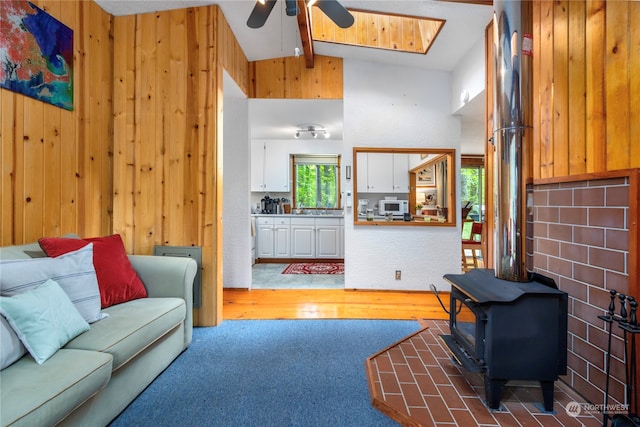 living room featuring a wood stove, ceiling fan, lofted ceiling with skylight, hardwood / wood-style floors, and sink