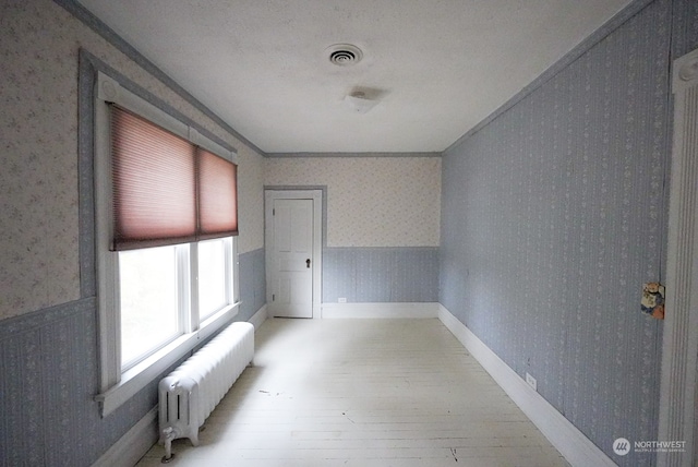 spare room with light hardwood / wood-style floors, a textured ceiling, and radiator heating unit