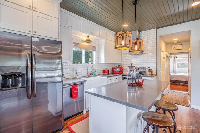 kitchen featuring white cabinetry, hanging light fixtures, stainless steel appliances, light hardwood / wood-style flooring, and a kitchen island