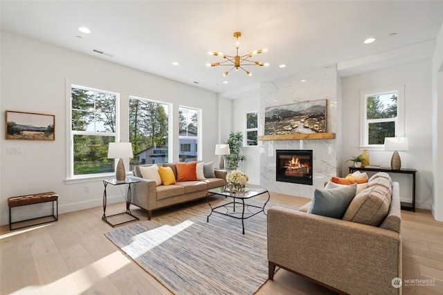 living room with an inviting chandelier, light hardwood / wood-style flooring, a high end fireplace, and a wealth of natural light