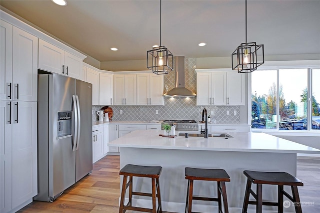 kitchen featuring white cabinetry, light hardwood / wood-style flooring, wall chimney range hood, and appliances with stainless steel finishes