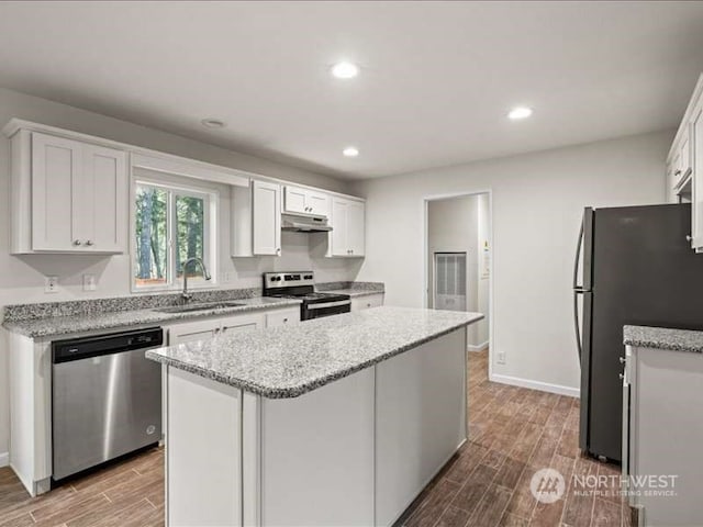 kitchen with hardwood / wood-style floors, appliances with stainless steel finishes, sink, white cabinets, and a kitchen island