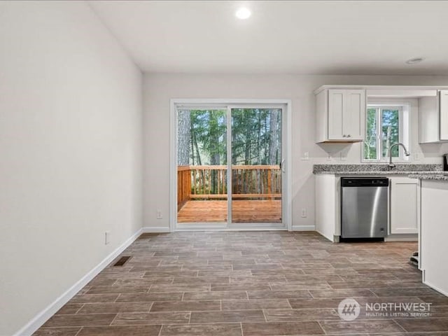 kitchen featuring plenty of natural light, white cabinetry, light stone countertops, and dishwasher