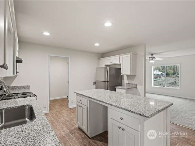 kitchen featuring ceiling fan, white cabinets, stainless steel fridge, light wood-type flooring, and light stone counters