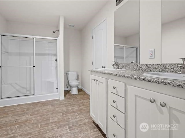 bathroom featuring toilet, double vanity, and a shower with shower door