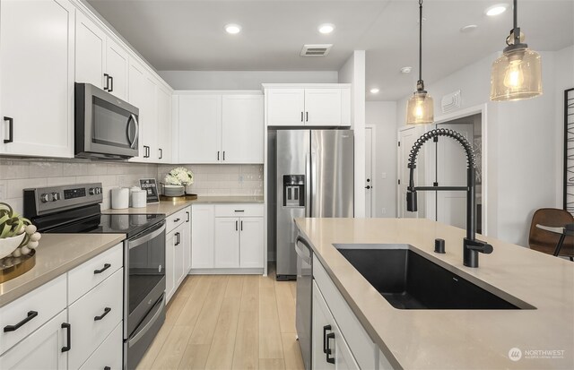 kitchen featuring sink, tasteful backsplash, pendant lighting, stainless steel appliances, and white cabinets