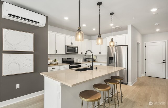 kitchen with appliances with stainless steel finishes, backsplash, white cabinets, a kitchen island with sink, and a wall unit AC