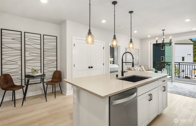 kitchen with pendant lighting, sink, dishwasher, white cabinetry, and an island with sink