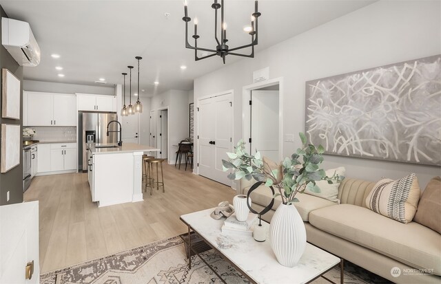 living room featuring sink, a wall mounted AC, a chandelier, and light hardwood / wood-style flooring