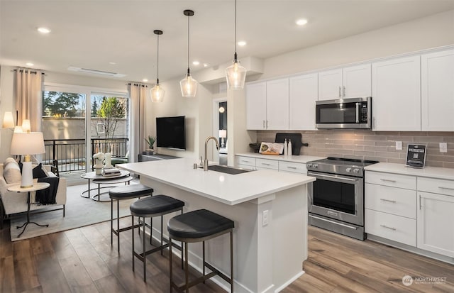 kitchen with appliances with stainless steel finishes, an island with sink, sink, white cabinets, and hanging light fixtures