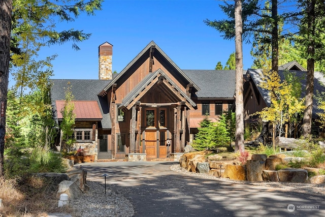 rustic home with a shingled roof, stone siding, and aphalt driveway