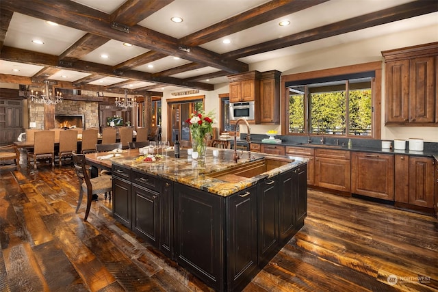 kitchen with a notable chandelier, dark wood finished floors, dark stone counters, a spacious island, and beam ceiling