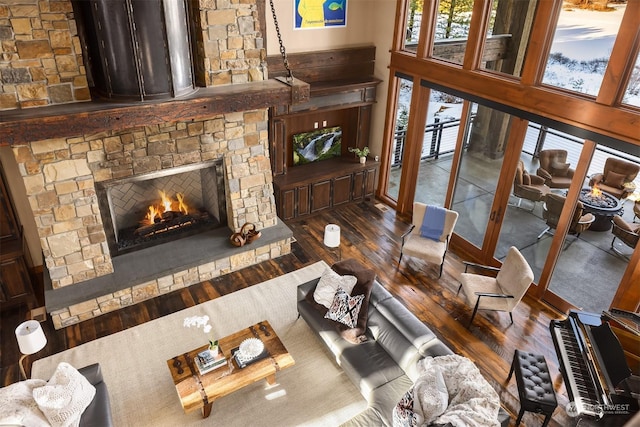 living room featuring a high ceiling, a stone fireplace, and wood finished floors
