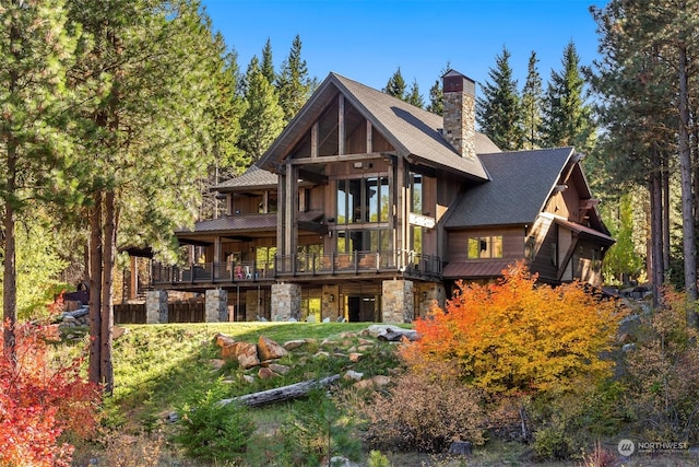 back of property featuring a chimney, a shingled roof, and stone siding