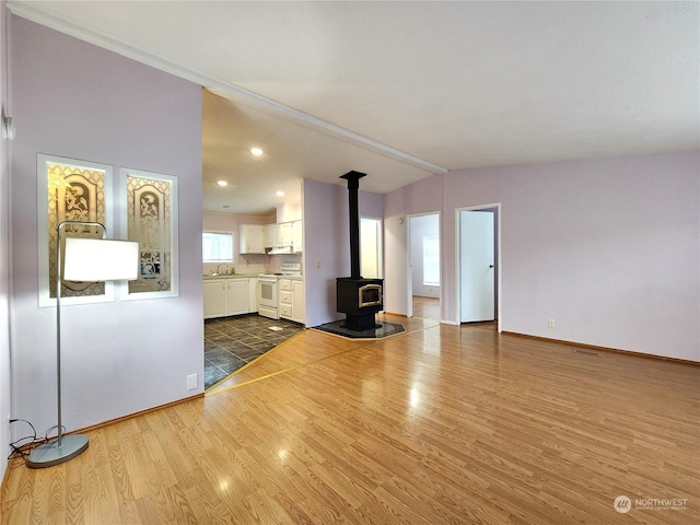 unfurnished living room featuring a wood stove, wood-type flooring, sink, and lofted ceiling