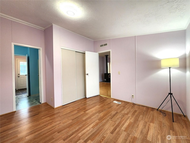 unfurnished bedroom with a textured ceiling, a closet, hardwood / wood-style floors, and crown molding