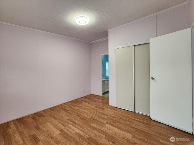 unfurnished bedroom with light hardwood / wood-style flooring, a closet, a textured ceiling, ensuite bathroom, and crown molding