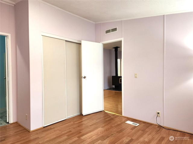 unfurnished bedroom with light hardwood / wood-style floors, crown molding, a wood stove, and a closet