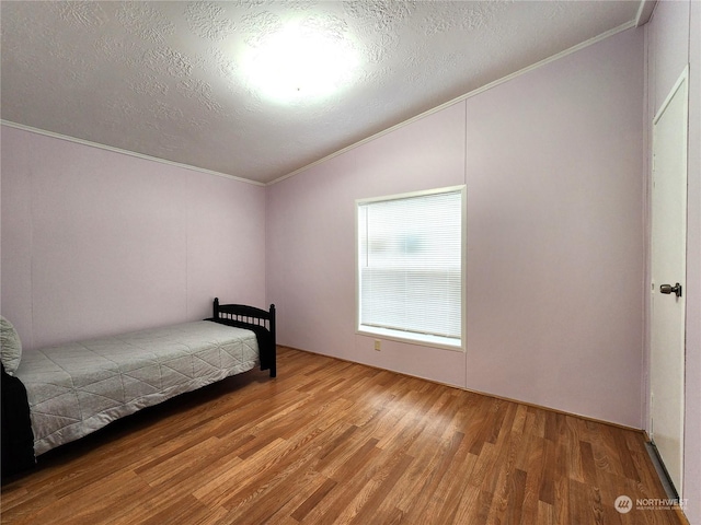 unfurnished bedroom featuring lofted ceiling, ornamental molding, a textured ceiling, and hardwood / wood-style floors