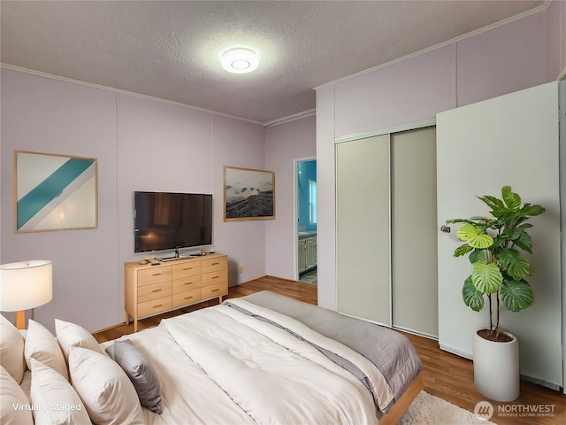 bedroom featuring hardwood / wood-style flooring, ensuite bath, a closet, a textured ceiling, and crown molding