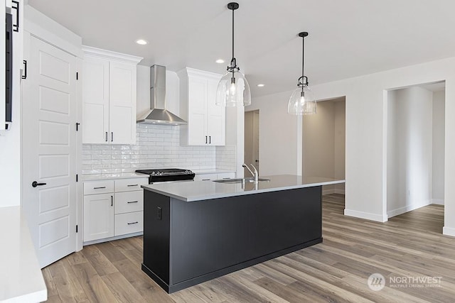 kitchen with pendant lighting, white cabinetry, wall chimney range hood, and an island with sink