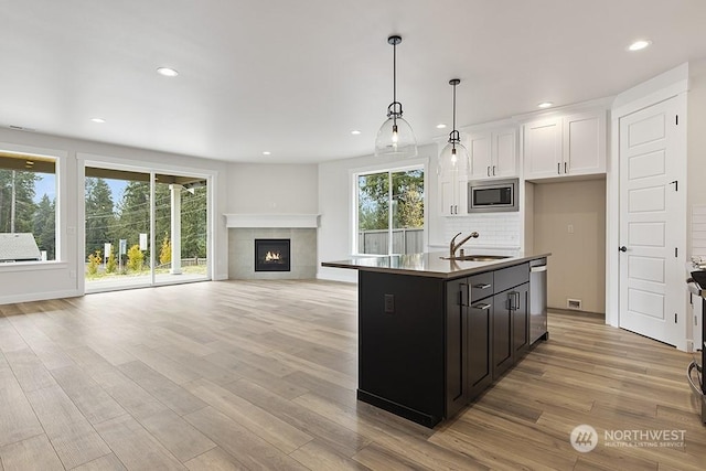 kitchen featuring sink, an island with sink, decorative light fixtures, decorative backsplash, and appliances with stainless steel finishes