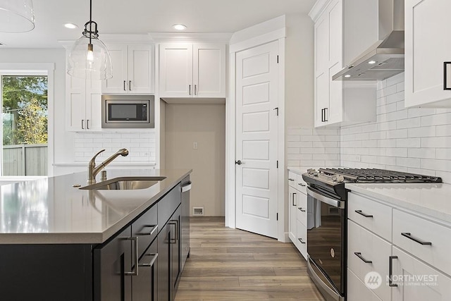 kitchen with appliances with stainless steel finishes, sink, wall chimney range hood, pendant lighting, and white cabinets