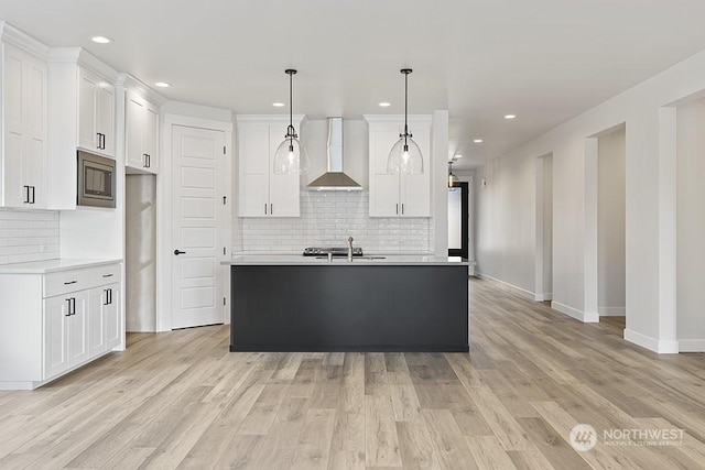 kitchen with white cabinets, hanging light fixtures, wall chimney exhaust hood, and a kitchen island with sink