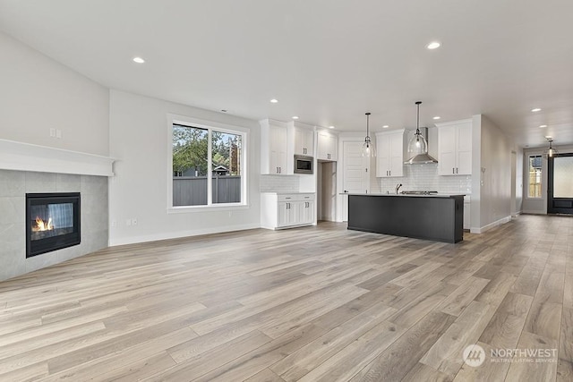 unfurnished living room with light hardwood / wood-style floors, sink, and a tiled fireplace