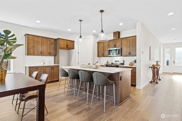 kitchen with a kitchen island, decorative light fixtures, backsplash, stainless steel appliances, and light wood-type flooring