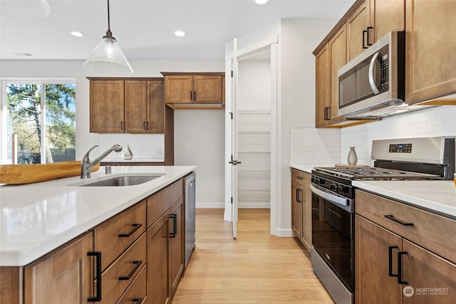 kitchen featuring sink, light hardwood / wood-style flooring, stainless steel appliances, decorative backsplash, and decorative light fixtures