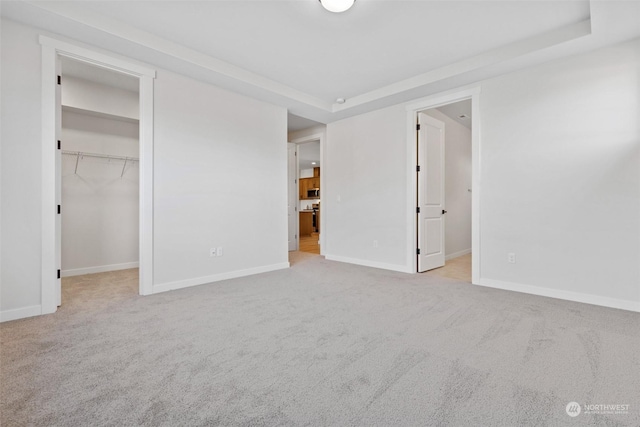 unfurnished bedroom with a walk in closet, a tray ceiling, light carpet, and a closet