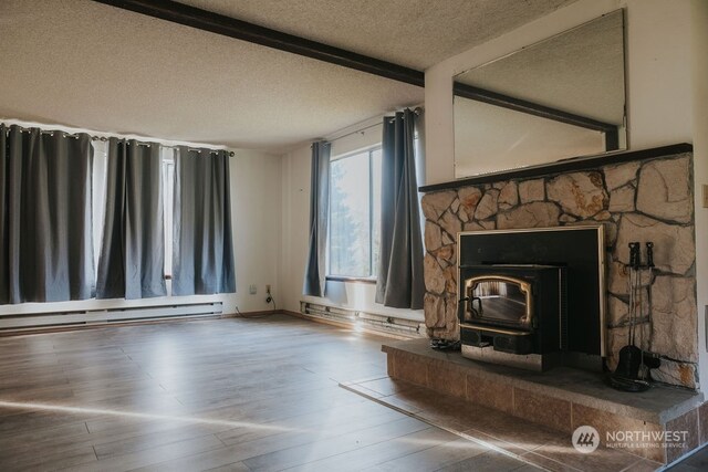 unfurnished living room featuring baseboard heating, a wood stove, wood-type flooring, a fireplace, and a textured ceiling