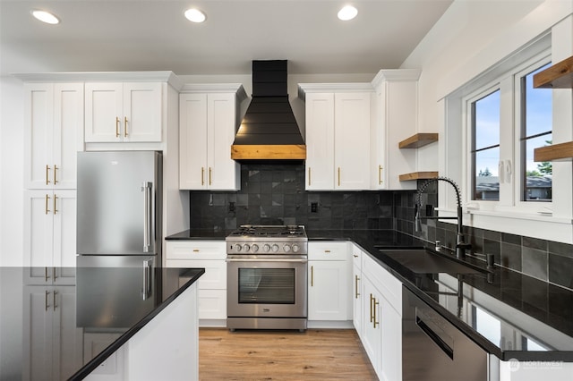 kitchen with custom exhaust hood, stainless steel appliances, sink, light hardwood / wood-style flooring, and backsplash