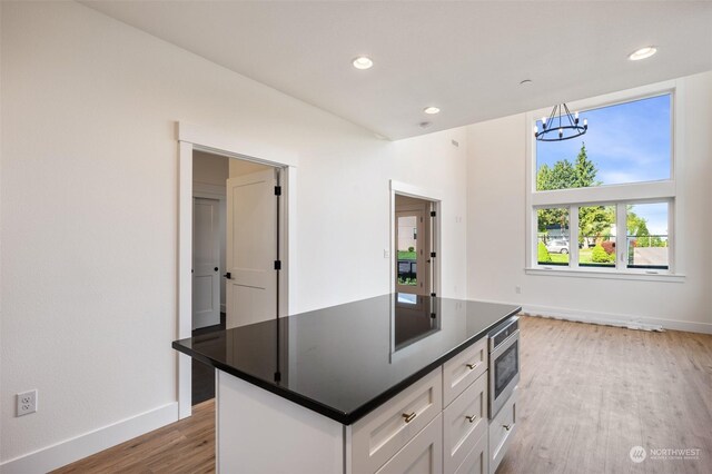 kitchen with light hardwood / wood-style flooring, white cabinets, wall oven, decorative light fixtures, and a kitchen island