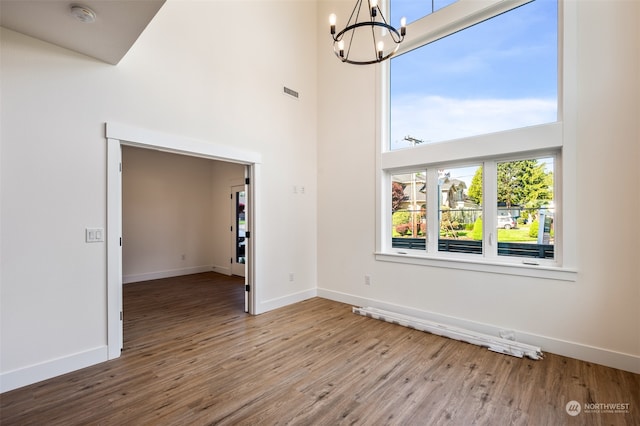 spare room featuring a chandelier, hardwood / wood-style flooring, and a towering ceiling