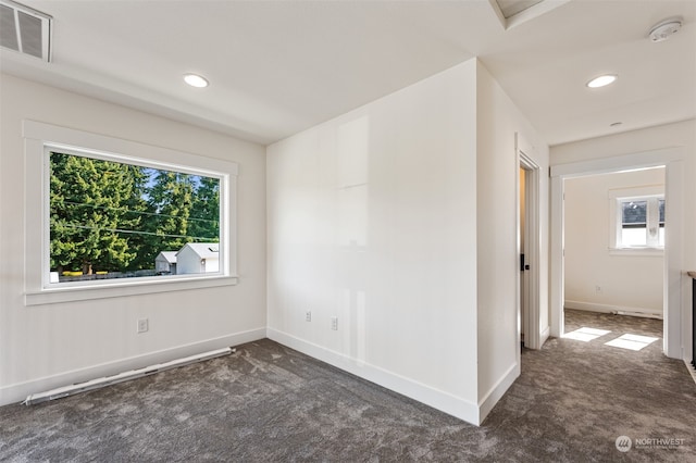 spare room featuring dark colored carpet and plenty of natural light