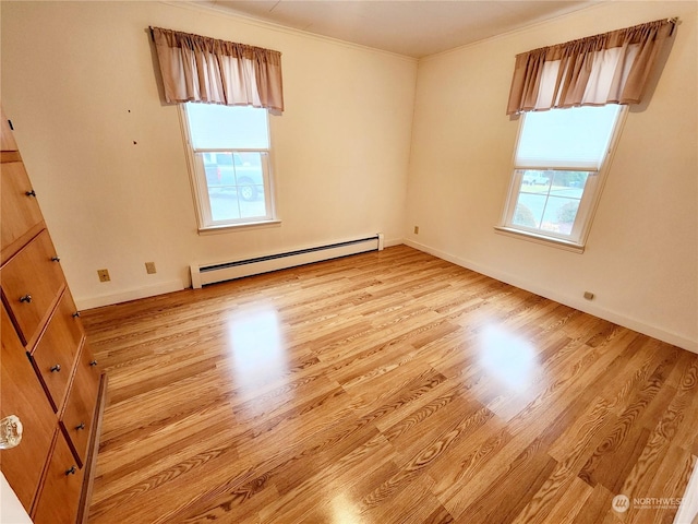 spare room featuring a healthy amount of sunlight, a baseboard heating unit, and light hardwood / wood-style flooring