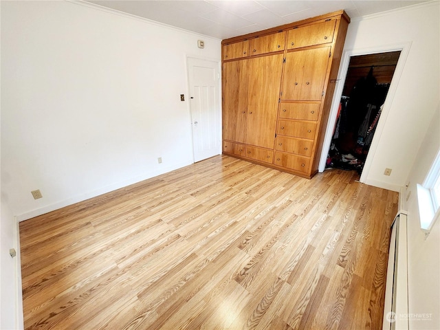 unfurnished bedroom featuring ornamental molding, light hardwood / wood-style floors, a closet, and baseboard heating