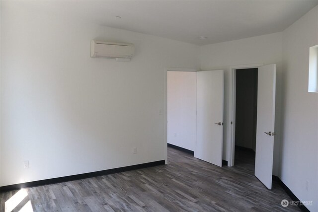 unfurnished bedroom featuring a wall mounted AC and dark hardwood / wood-style flooring