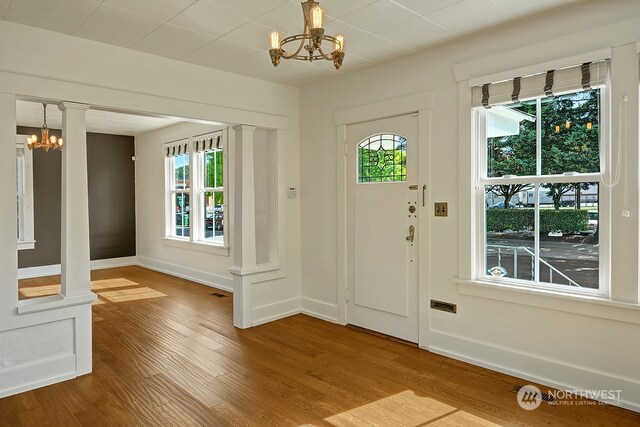 entryway with an inviting chandelier, wood-type flooring, decorative columns, and a healthy amount of sunlight