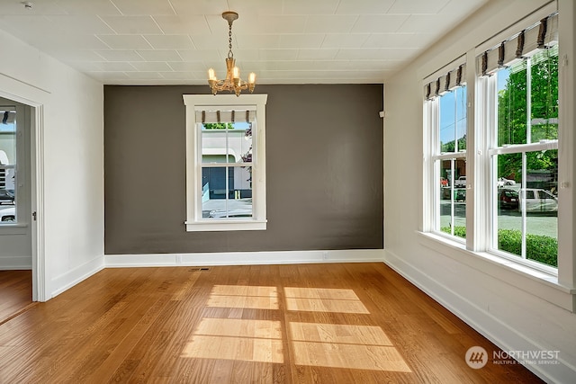 unfurnished dining area featuring an inviting chandelier and hardwood / wood-style floors