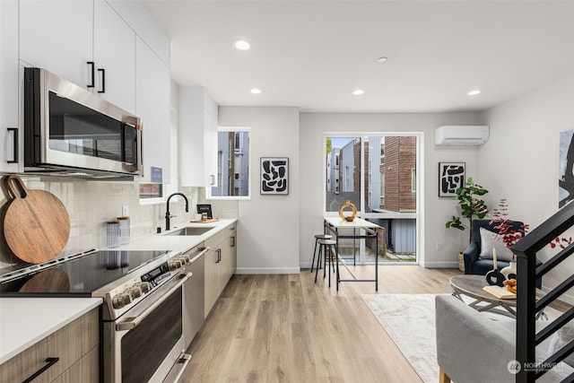 kitchen with sink, stainless steel appliances, a wall mounted AC, light hardwood / wood-style floors, and white cabinets