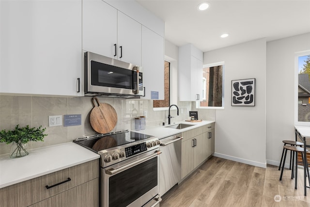 kitchen with appliances with stainless steel finishes, light wood-type flooring, tasteful backsplash, sink, and white cabinets